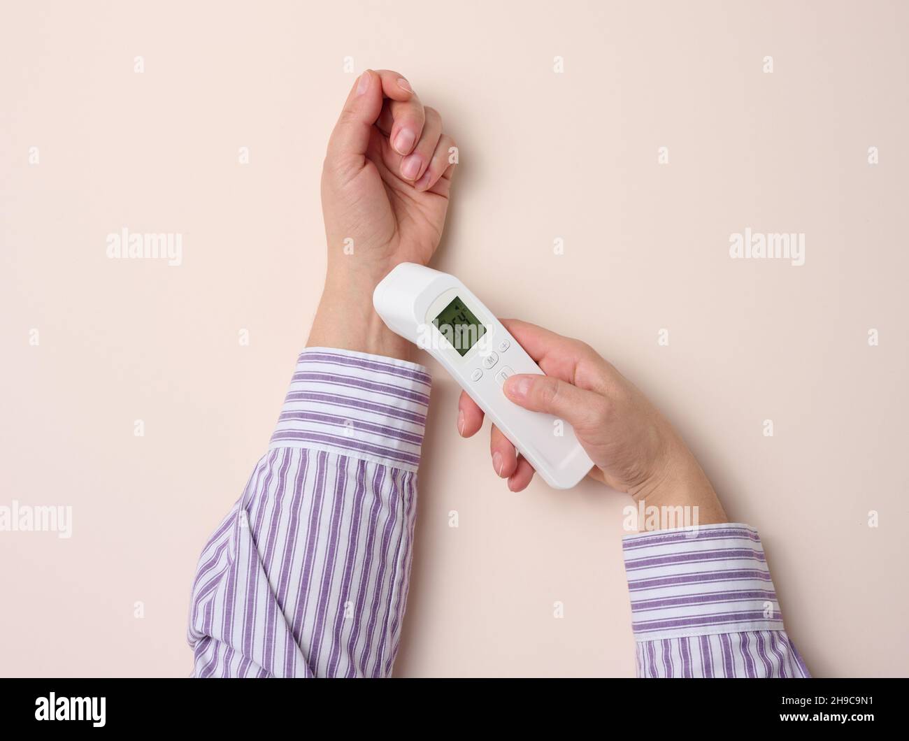 processus de mesure de la température corporelle au poignet avec un  thermomètre sans contact, fond beige Photo Stock - Alamy