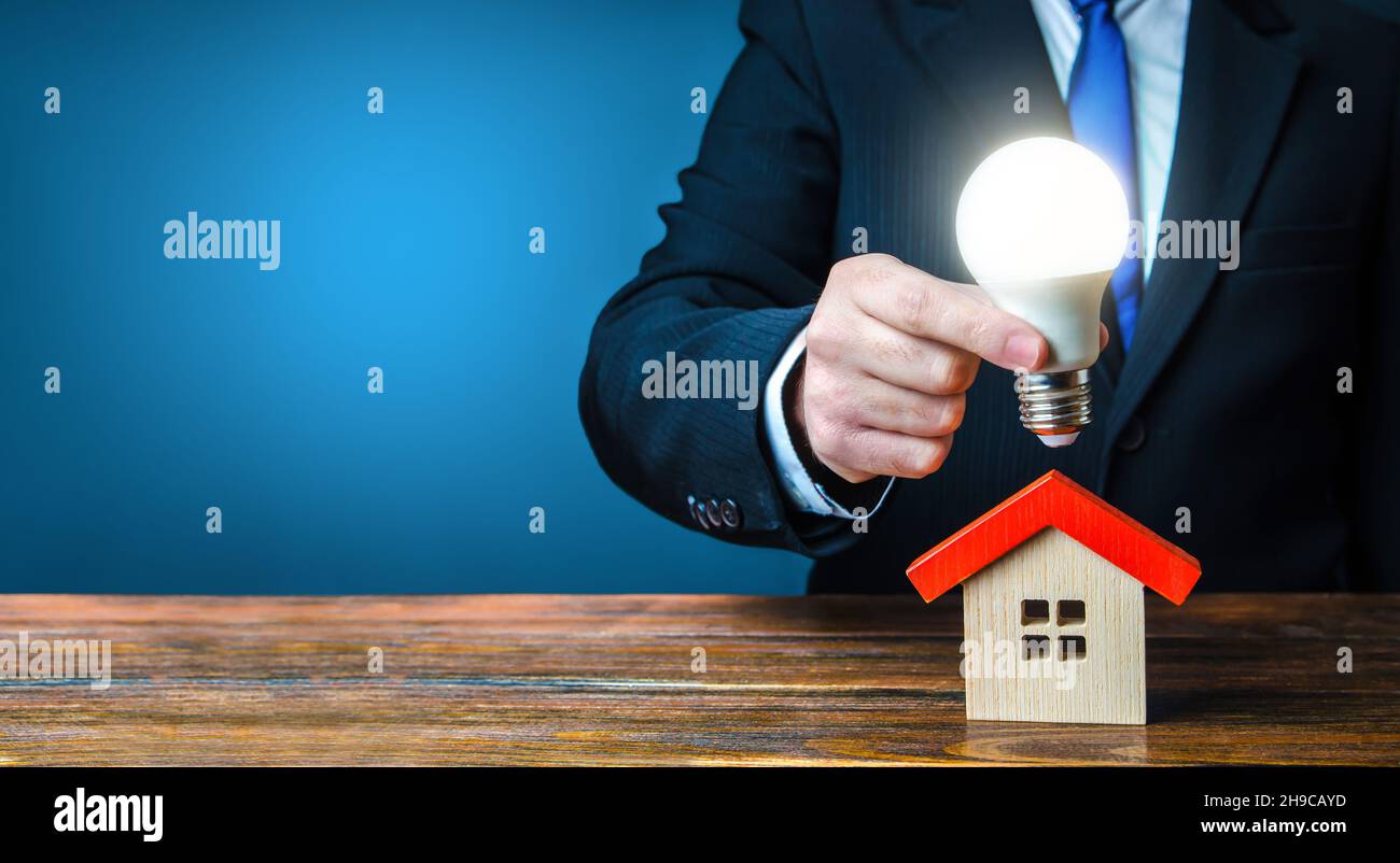 L'homme tient une ampoule lumineuse au-dessus de la maison.Concept de maison intelligente.Fourniture de logements avec électricité et communications.Traiter le contrat avec les Banque D'Images