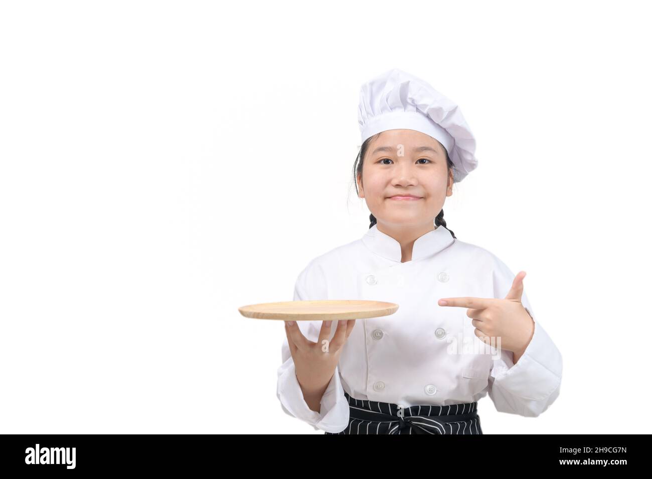 le chef mignon tient une assiette en bois et pointe son doigt sur une assiette isolée sur fond blanc. concept de présentation du menu de la nourriture Banque D'Images