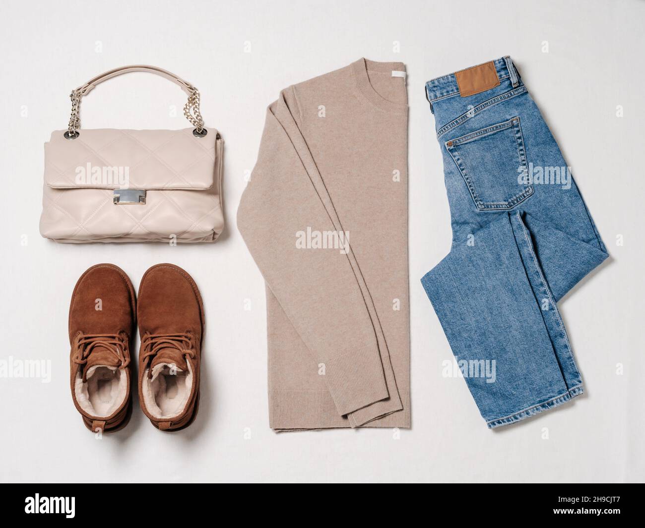 Couvre-lit confortable tendance en hiver.Chandail beige cachemire, Jean bleu, bottes en daim Chukka marron châtaignier avec fourrure de laine et sac beige neutre sur fond blanc.Tenue chic et décontractée pour femme.Vue de dessus Banque D'Images