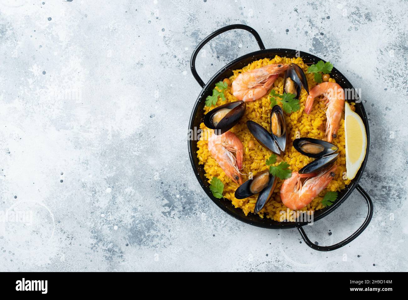 Paella traditionnelle espagnole de fruits de mer en casserole avec pois chiches, crevettes, moules, calmars sur fond de béton gris clair. Vue de dessus avec espace de copie. Banque D'Images