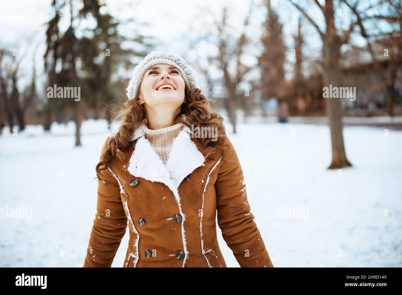 bonne femme élégante dehors dans le parc de la ville en hiver dans un bonnet tricoté et un manteau de peau de mouton. Banque D'Images