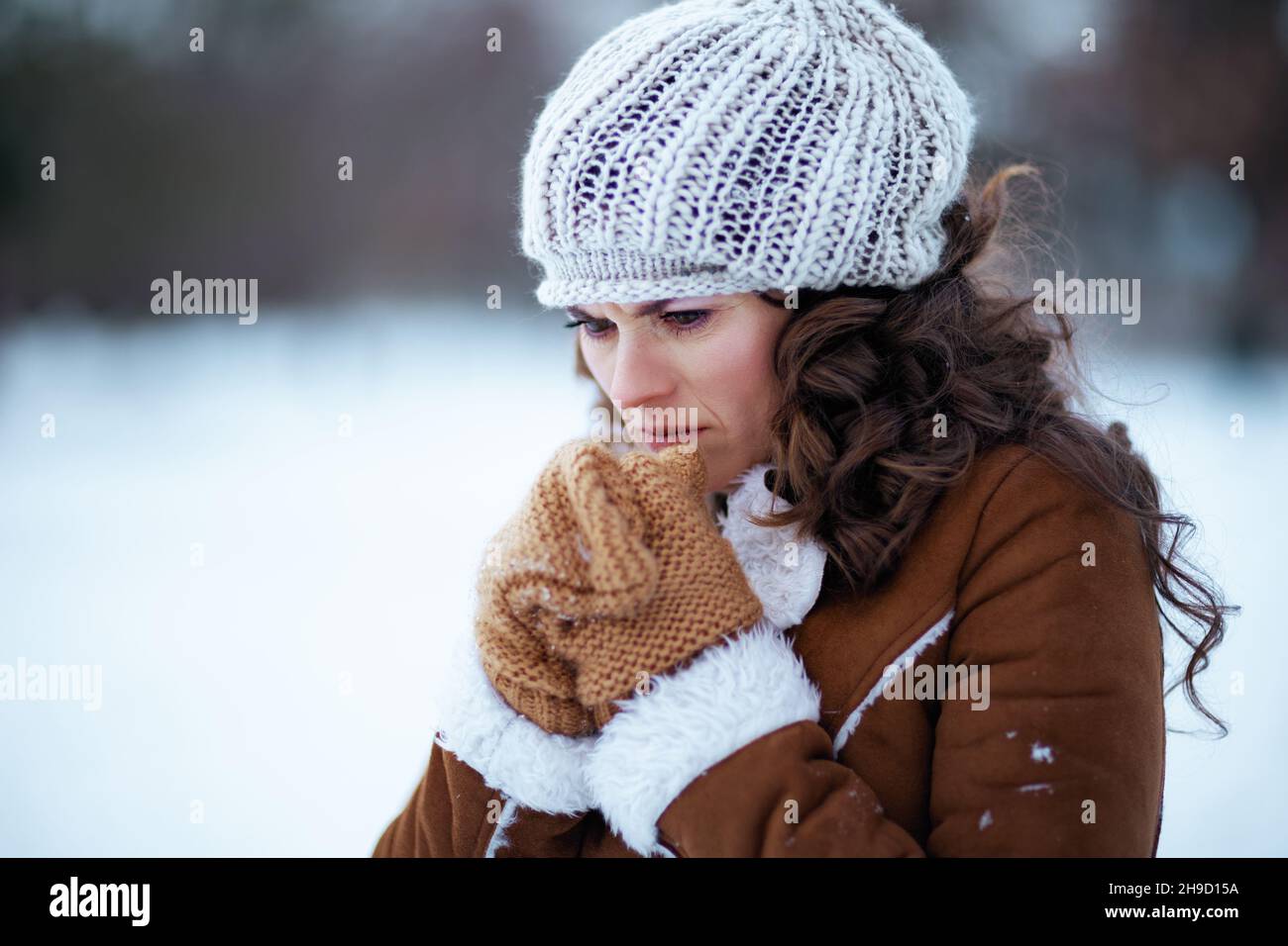 femme moderne stressée avec des moufles dans un bonnet tricoté et un  manteau de peau de mouton dehors dans le parc de la ville en hiver Photo  Stock - Alamy