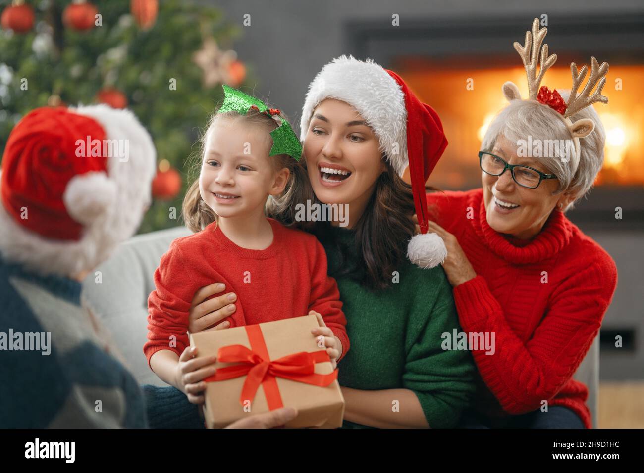 Joyeux Noël et joyeuses fêtes ! Grand-mère, grand-père, mère et enfant échangeant des cadeaux. Parents et filles s'amuser près de l'arbre à l'intérieur. Affectueux famil Banque D'Images