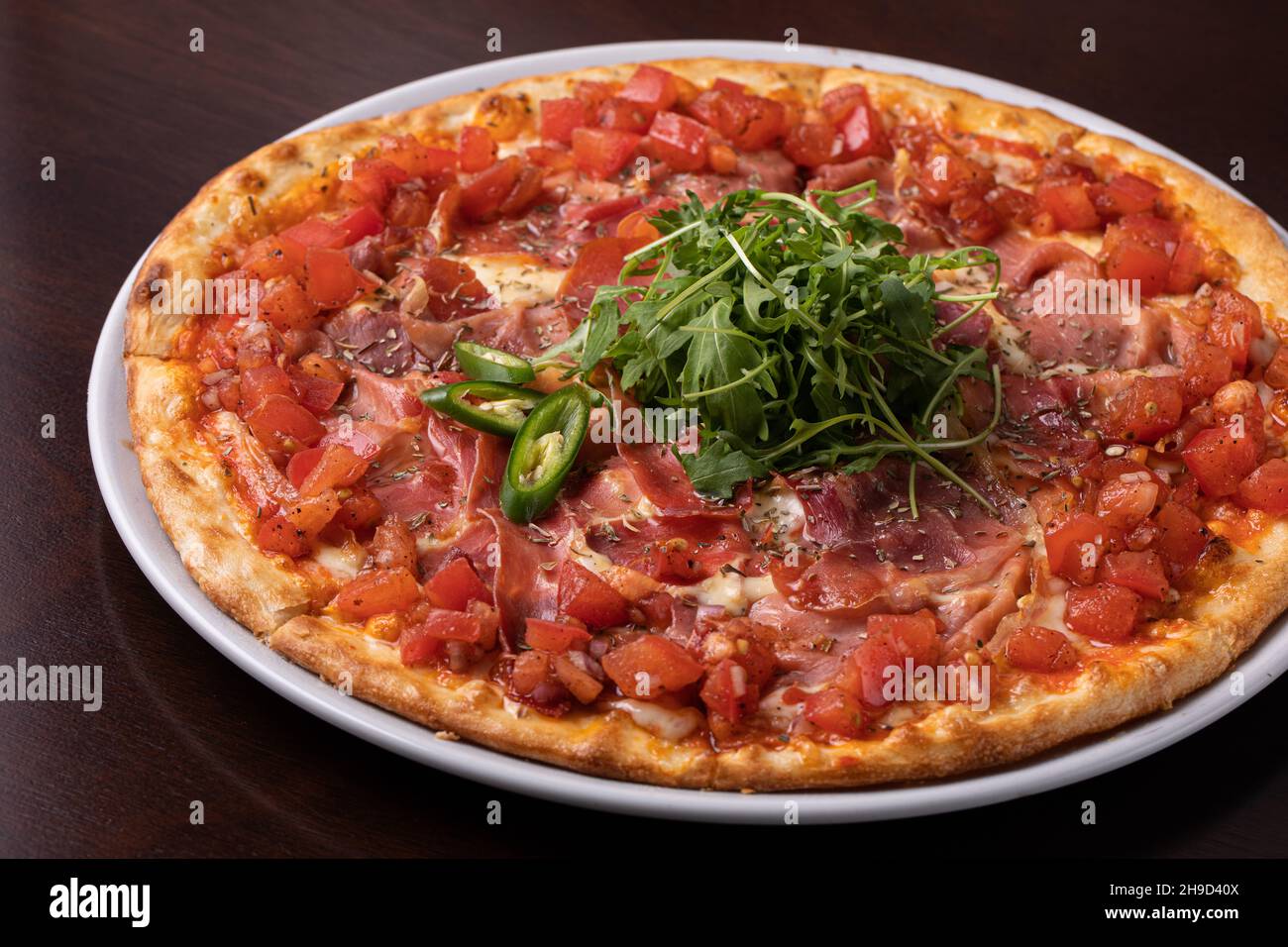 pizza au jambon avec tomates, fromage et nappée de piments verts et d'arugula Banque D'Images