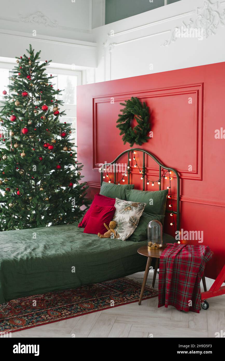 Un lit avec des oreillers verts et un drap à l'intérieur d'une chambre de  Noël sur le fond d'un mur rouge avec une couronne.Il y a un arbre de Noël b  Photo