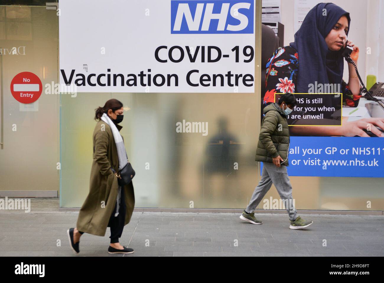 Piétons passant par le centre de vaccination NHS Covid-19 à Westfield, Stratford.Le Royaume-Uni réintroduit les restrictions en cas de pandémie suite à l'émergence de la variante Omicron COVID-19.Les jabs de rappel seront disponibles en janvier. Banque D'Images