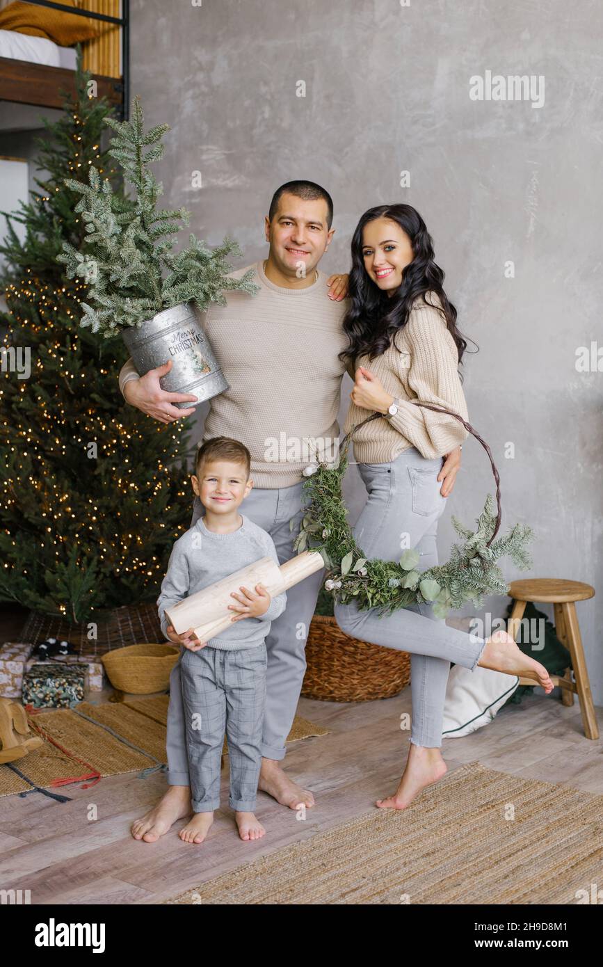 Maman et papa souriants avec leur petit fils sont debout à l'arbre de Noël décoré à la maison.Une famille heureuse fête Noël ou le nouvel an Banque D'Images