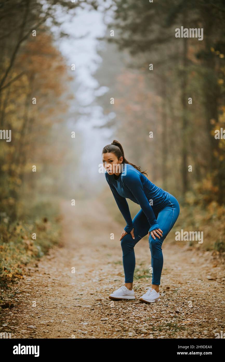 Une jolie jeune femme fait une pause lors d'un exercice en plein air sur le sentier forestier à l'automne Banque D'Images