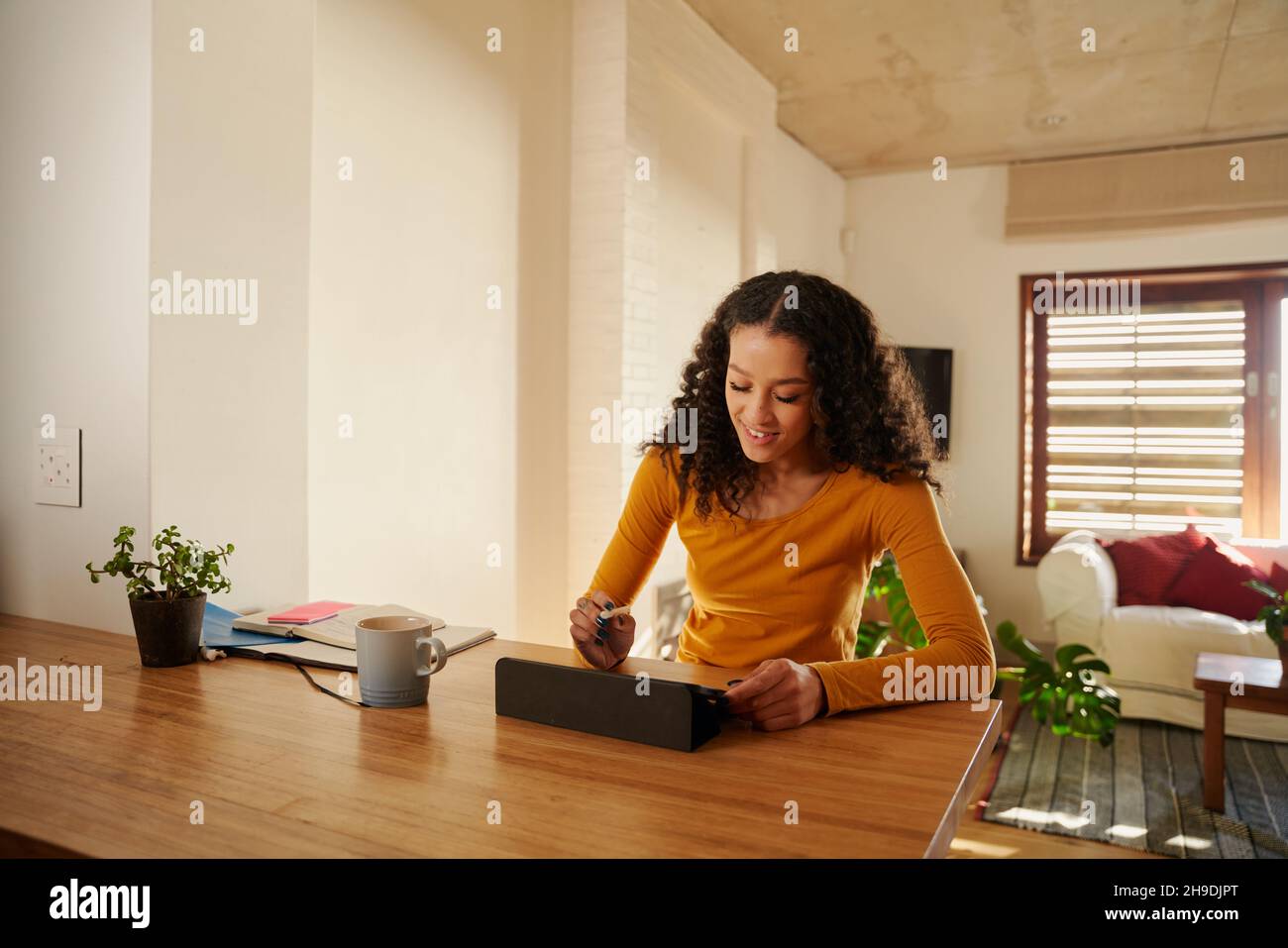 Jeune femme adulte multi-culturelle souriant en utilisant sa tablette électronique à son comptoir de cuisine moderne.Travail à distance Banque D'Images