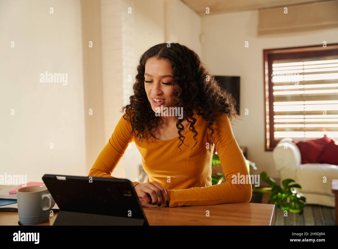 Jeune adulte multiculturel souriant lors d'un appel en ligne à l'aide de sa tablette électronique au comptoir de sa cuisine moderne Banque D'Images