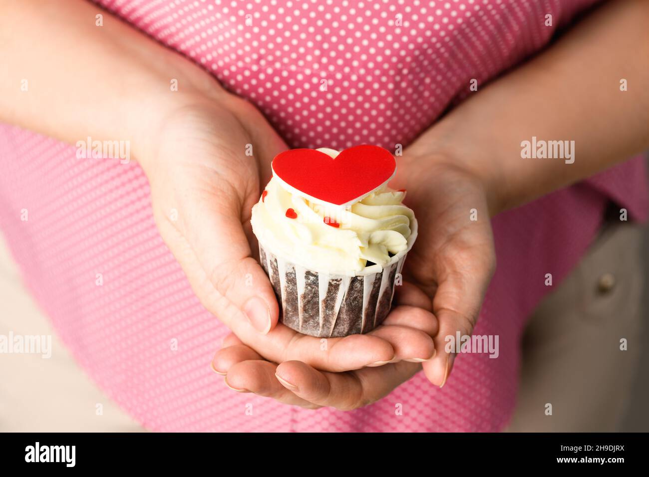 Gâteau en forme de coeur dans les mains de fille sur fond rose.Cupcake en gros plan en forme de coeur Banque D'Images