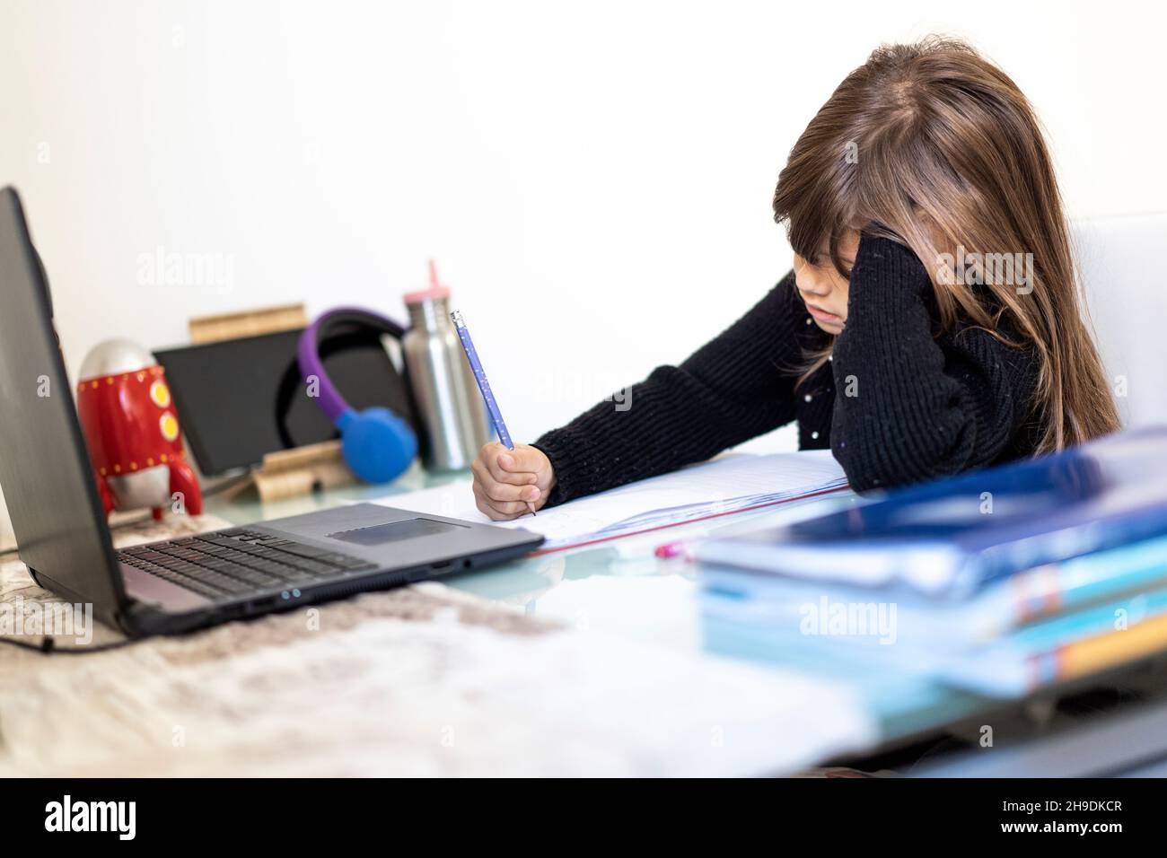 Enfant écolier fatigué fille à la maison avec un ordinateur portable pour la connexion à distance avec ses camarades de classe et le professeur - ennuyé petite fille apprenant en utilisant Internet le Banque D'Images