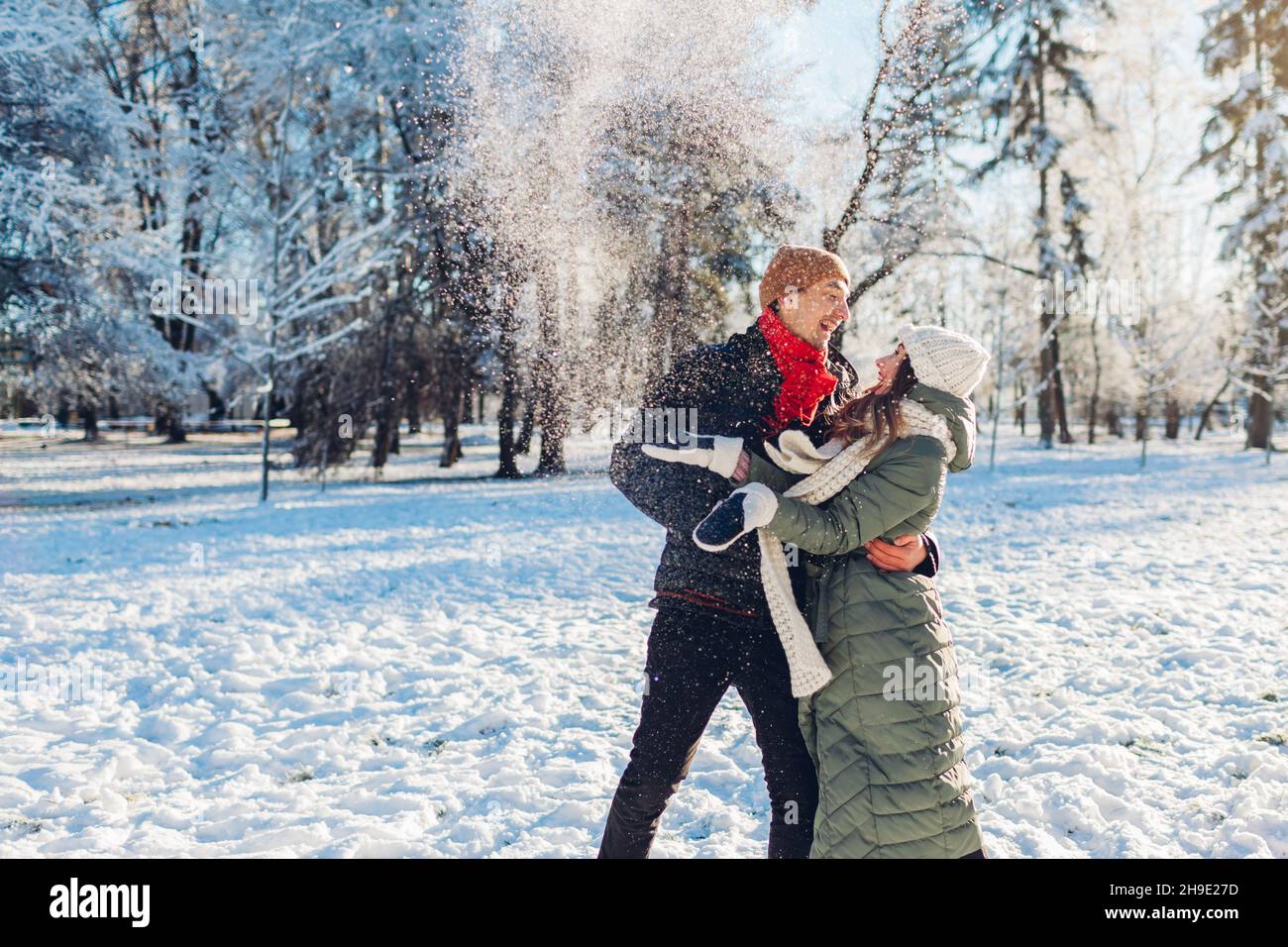 Joyeux jeune couple aimant jouant avec la neige le jetant dans le parc d'hiver.Homme et femme s'amusant à l'extérieur. Banque D'Images