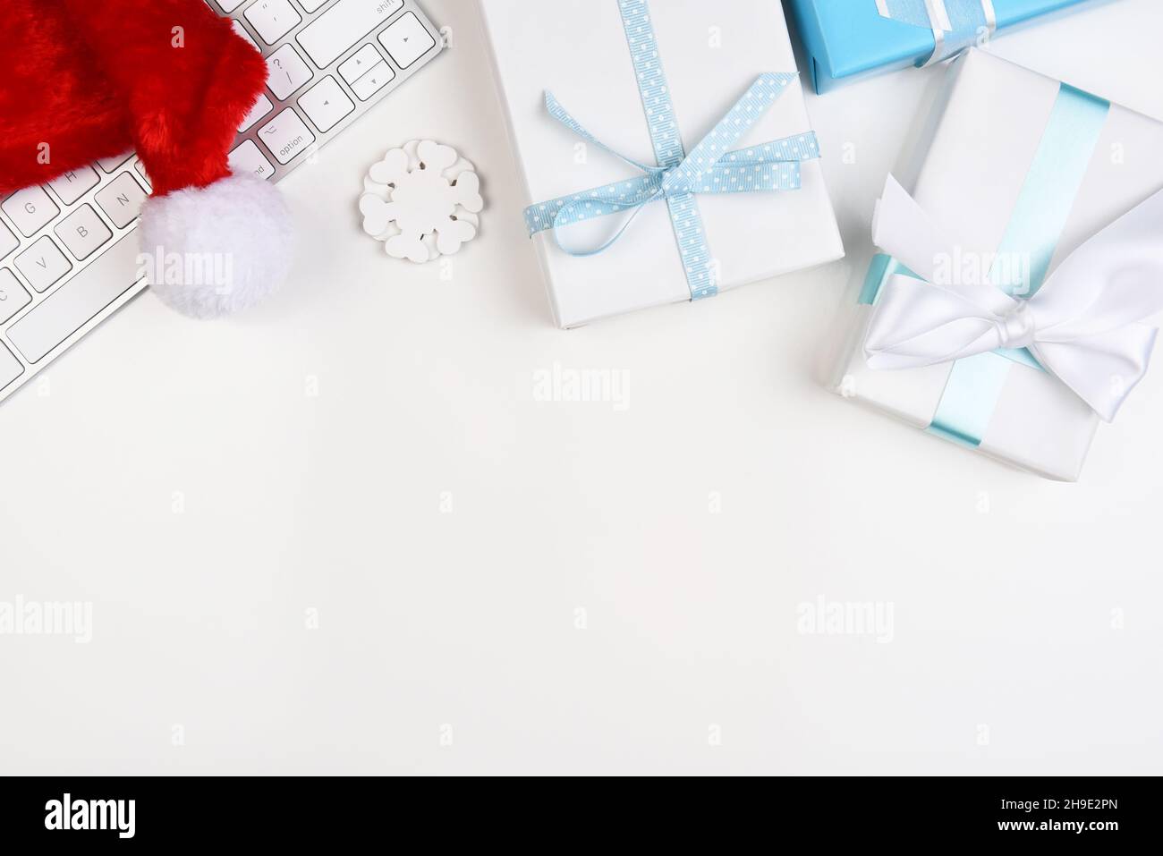 Concept de Noël à plat.Un clavier d'ordinateur, Santa Hat et papier blanc et bleu enveloppé présente avec un espace de copie dans la moitié inférieure de l'image. Banque D'Images