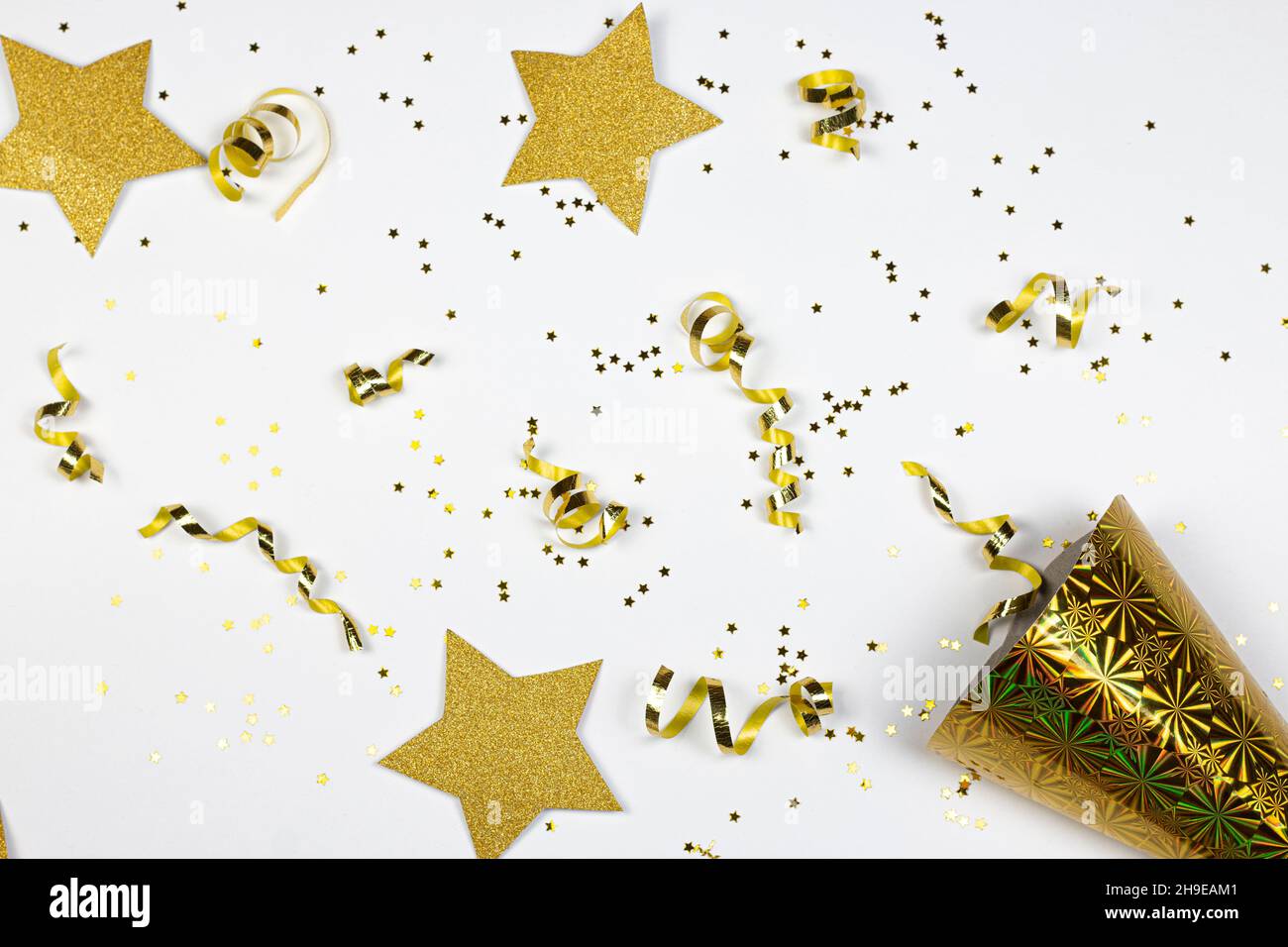 Étoiles scintillantes, confettis dorés et chapeau de fête en papier jaune sur fond blanc.Pose à plat.Concept de fête. Banque D'Images