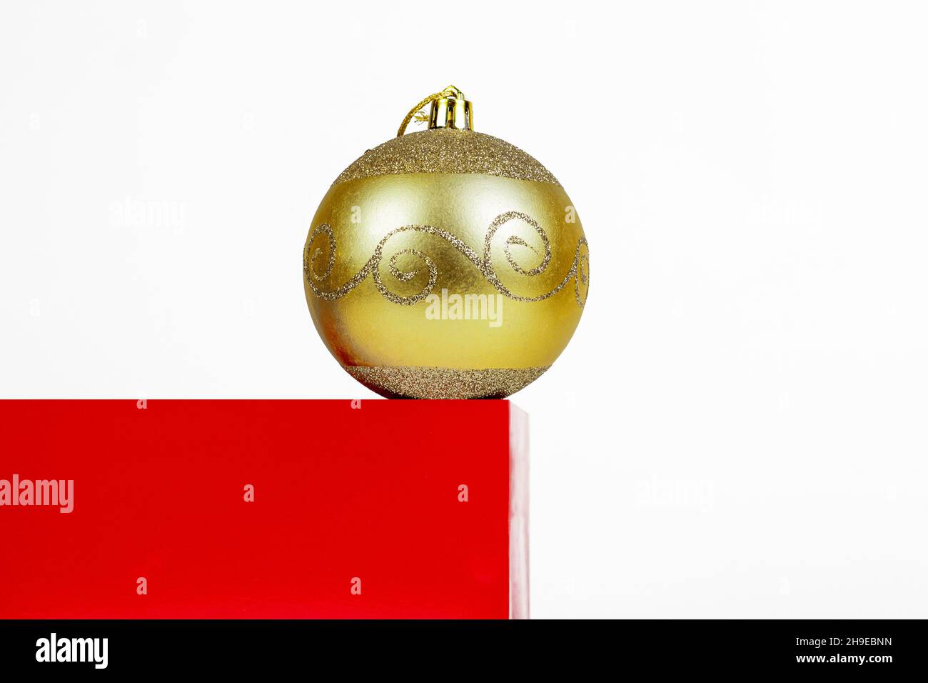 Composition de Noël minimale.Podium en forme de cube rouge avec boule de Noël jaune sur fond blanc avec espace de copie. Banque D'Images