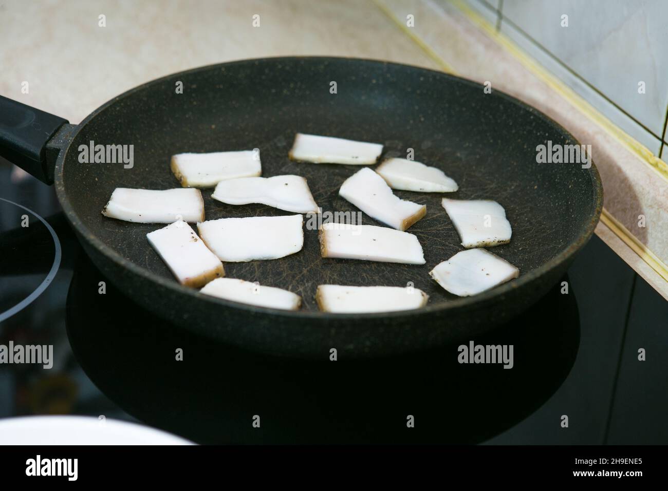 Le processus de cuisson des œufs brouillés avec du saindoux et de la saucisse.L'homme prépare deux portions.Les morceaux de bacon sont frits dans une poêle. Banque D'Images