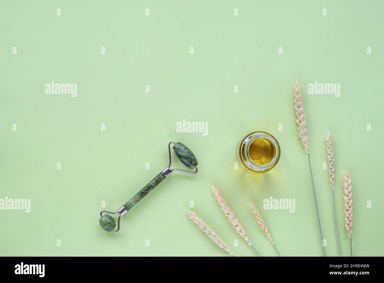 Sérum cosmétique en bouteille de verre, rouleau facial et épis de blé sur fond vert clair.Soins de la peau, concept de cosmétiques naturels biologiques.Vue de dessus, plat l Banque D'Images
