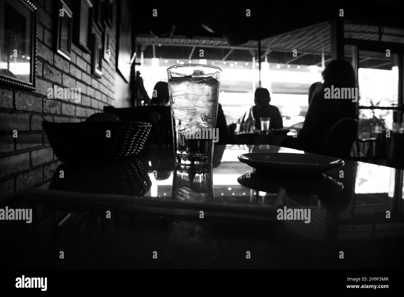 Image en noir et blanc d'un verre d'eau et d'une table dans un restaurant.Arrière-plan de mise au point douce. Banque D'Images