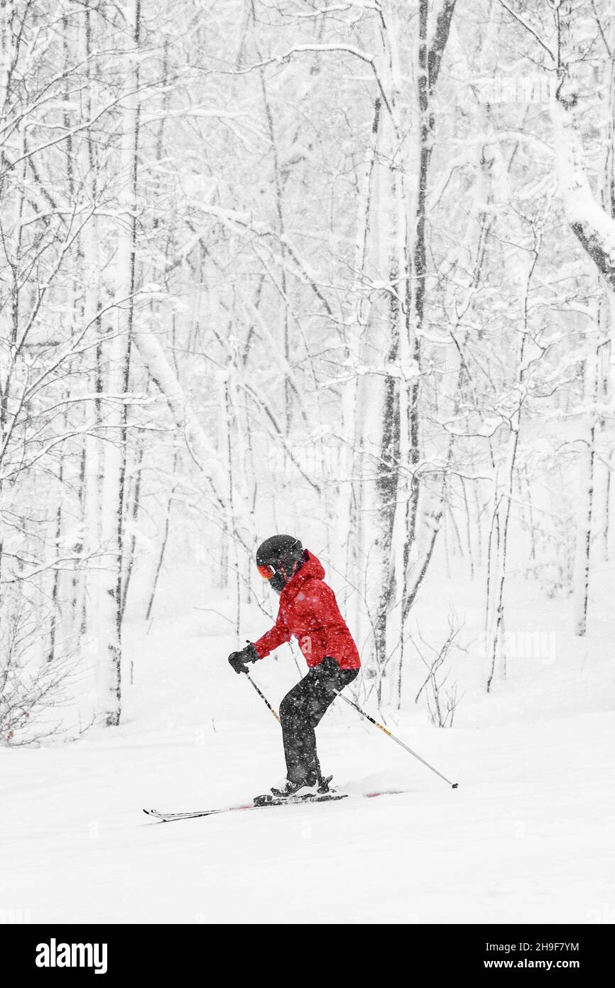 Ski alpin.Femme skieur qui va rapidement à la botte contre la neige a couvert les arbres arrière-plan pendant la tempête de neige d'hiver.Femme en blouson rouge et lunettes de protection.Hiver Banque D'Images