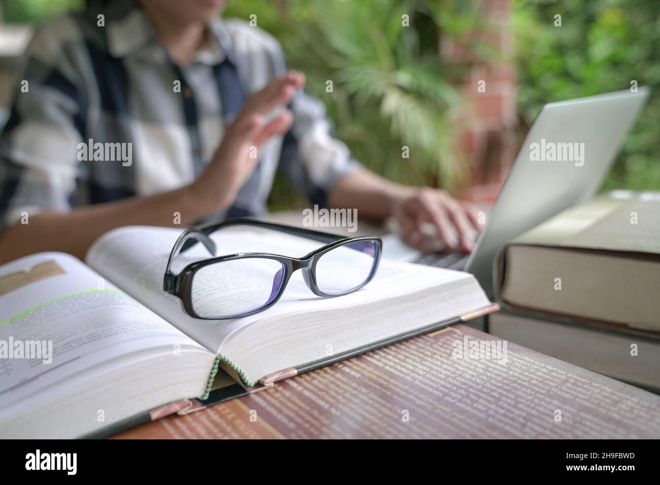 Livres sur table avec femme sur appel vidéo en ligne à l'arrière-plan.Mise au point sélective sur les lunettes. Banque D'Images