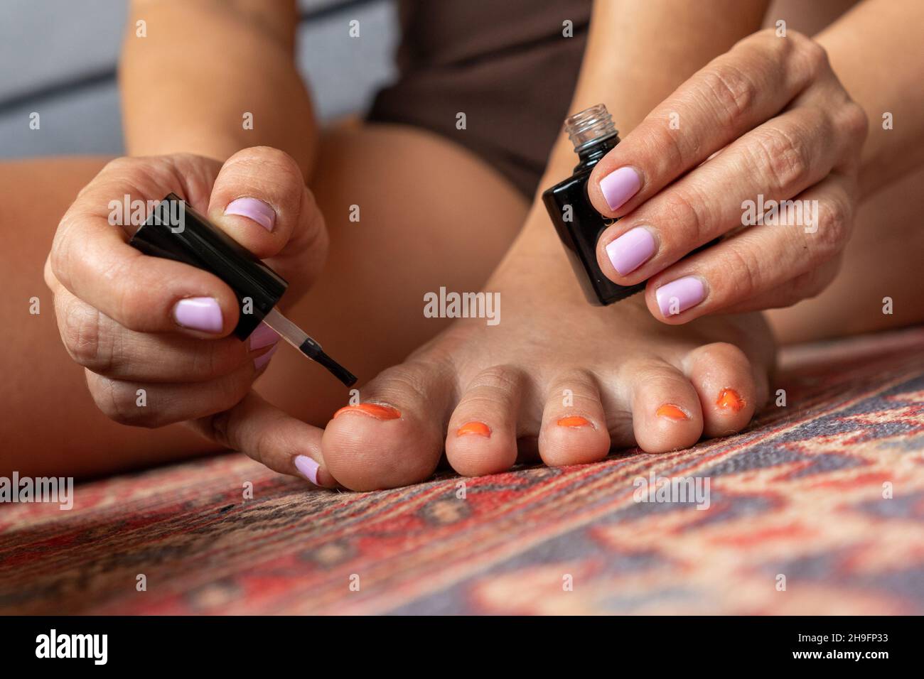 Femme aux pieds laids peignant ses ongles avec vernis à ongles orange Banque D'Images