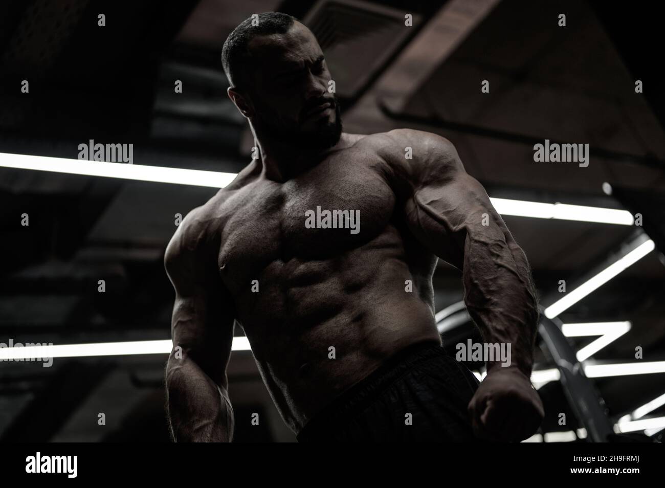 jeune homme robuste barbu avec corps bodybuilder dans la salle de sport de nuit sombre Banque D'Images