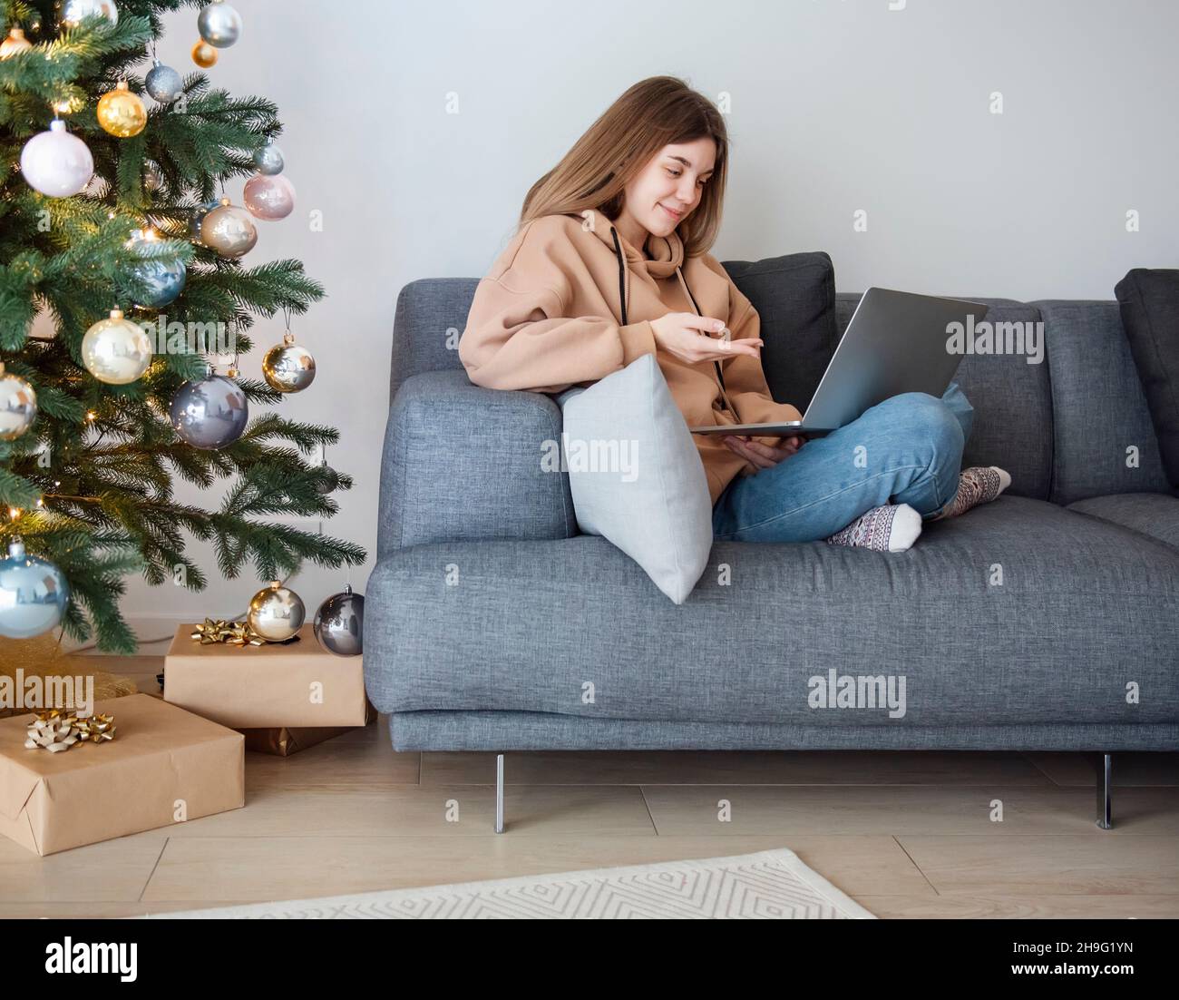 Adolescente avec ordinateur portable sur un canapé dans la salle de séjour près de l'arbre de Noël Banque D'Images