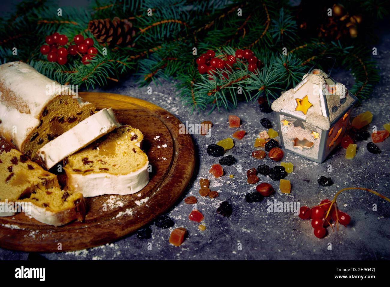 Composition en Chirstmass.Stollen sur un plateau en bois, fruits confits, raisins secs et baies de viburnum avec branches d'arbre de Noël sur un fond fixé. Banque D'Images