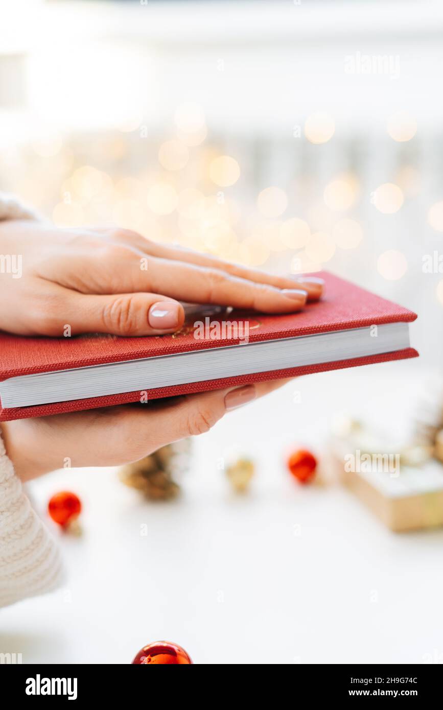 Un livre rouge entre les mains d'une jeune fille sur fond de cadeaux et de jouets de Noël, un bokeh garland. Le concept de Noël Banque D'Images