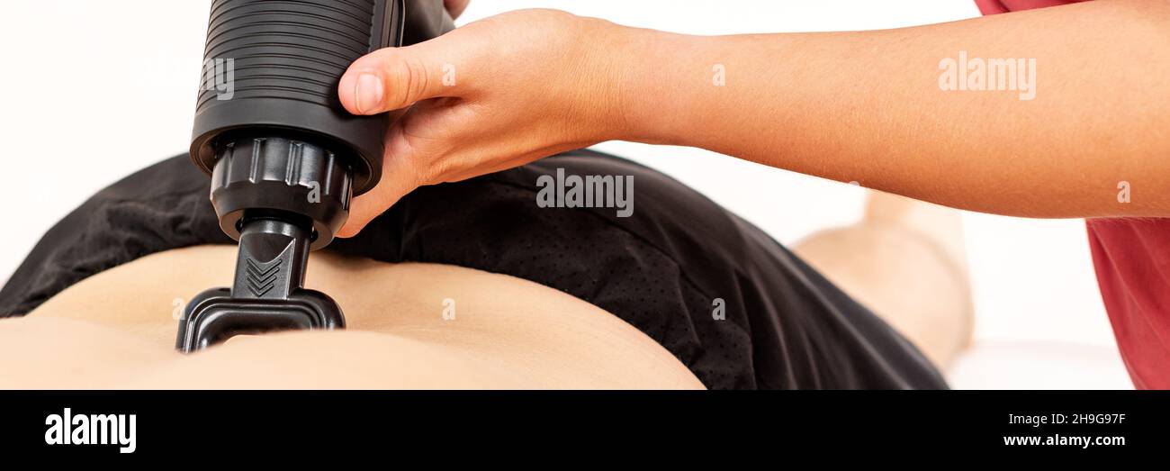 Bannière pistolet de massage.Une jeune physiothérapeute féminine utilise un appareil de massage portatif pour soulager les douleurs dans le bas du dos pendant la séance de physiothérapie. Banque D'Images