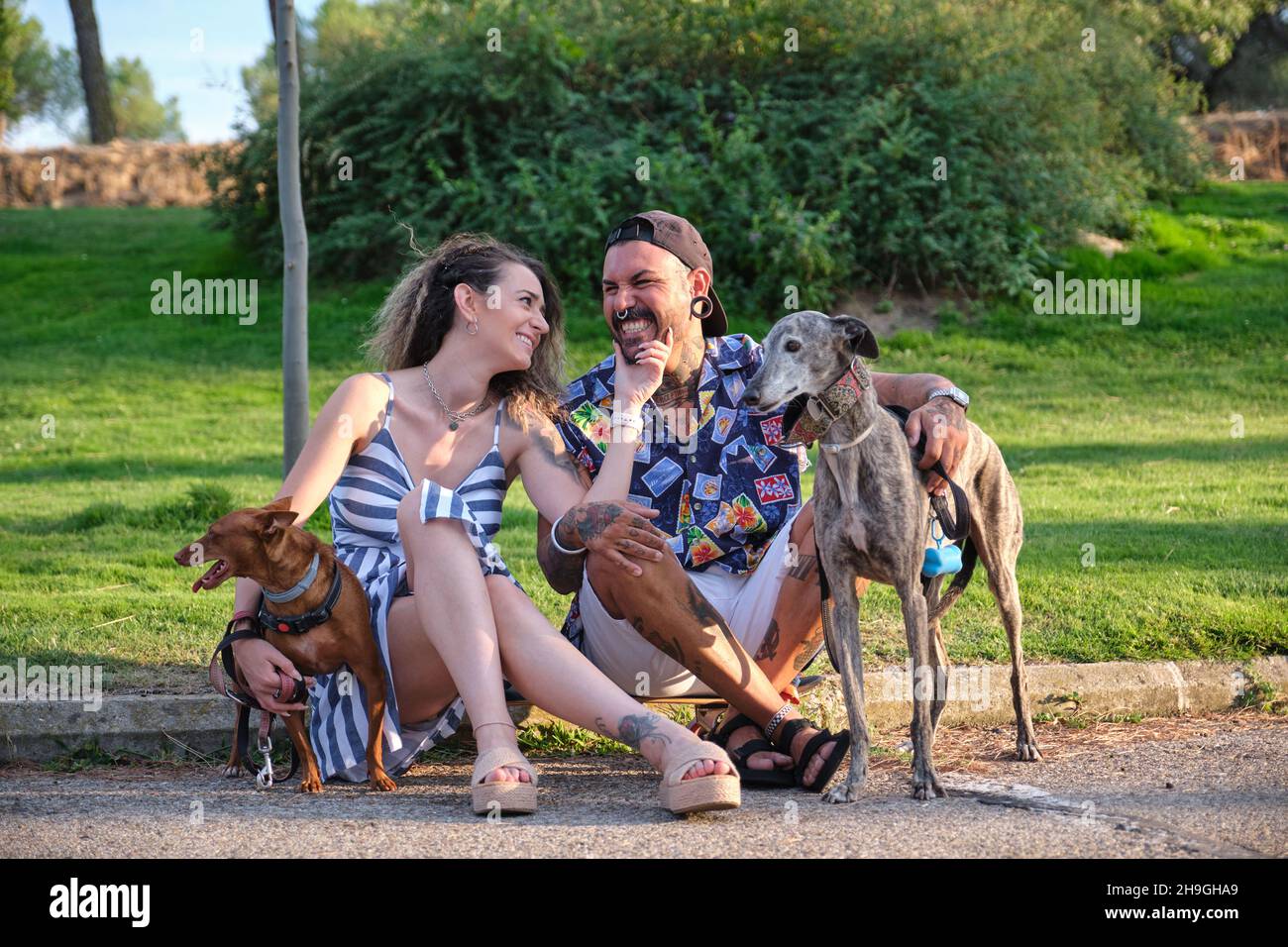 Jeune couple tatoué embrassant et assis avec leurs chiens. Banque D'Images
