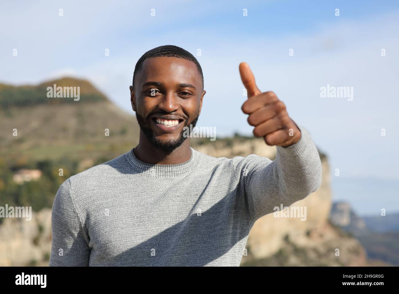 Homme heureux avec la peau noire gestante pouce vers le haut dans la montagne Banque D'Images