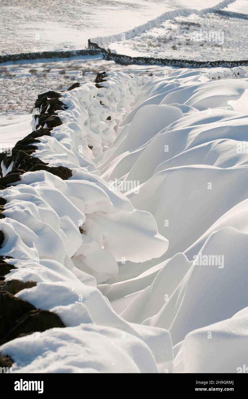 De neige formé par le vent neige soufflée à côté d'un mur de pierres sèches, Peak District, Derbyshire, Royaume-Uni Banque D'Images