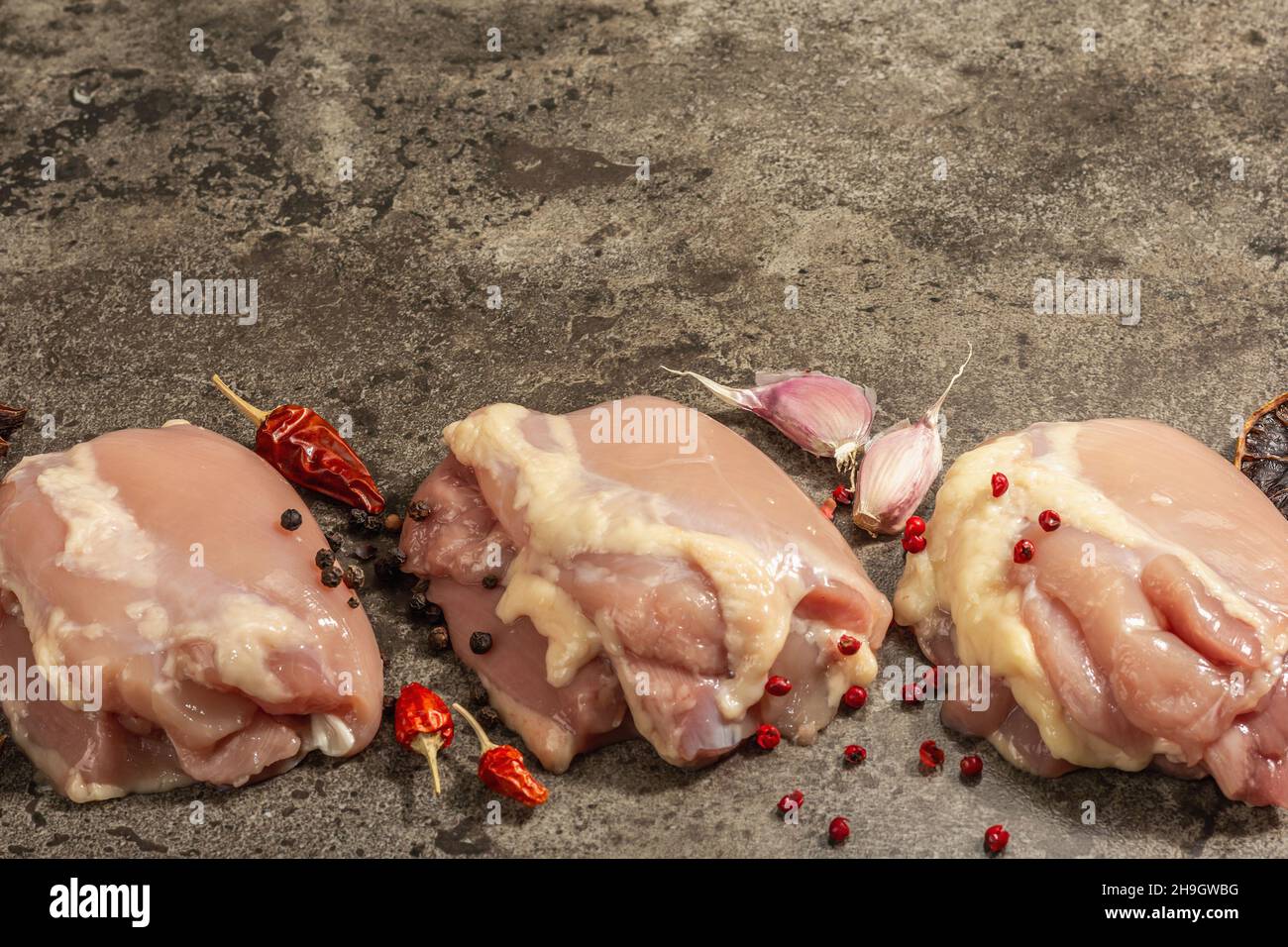 Cuisse de poulet crue sans os ni peau.Un ingrédient utile pour préparer des aliments sains, des épices, de l'ail.Arrière-plan en pierre sombre, espace de copie Banque D'Images