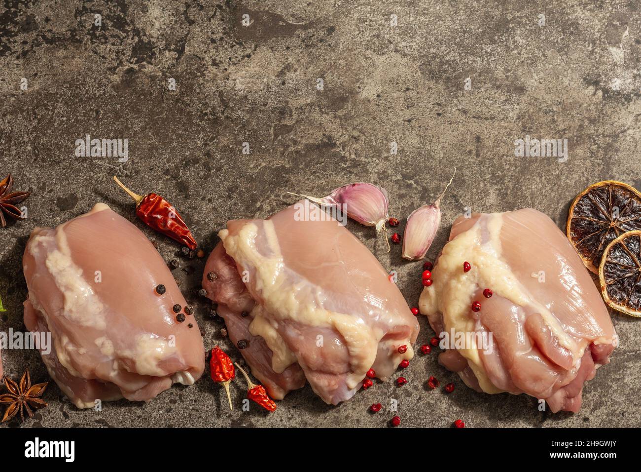 Cuisse de poulet crue sans os ni peau.Un ingrédient utile pour préparer des aliments sains, des épices, de l'ail.Arrière-plan en pierre sombre, vue du dessus Banque D'Images