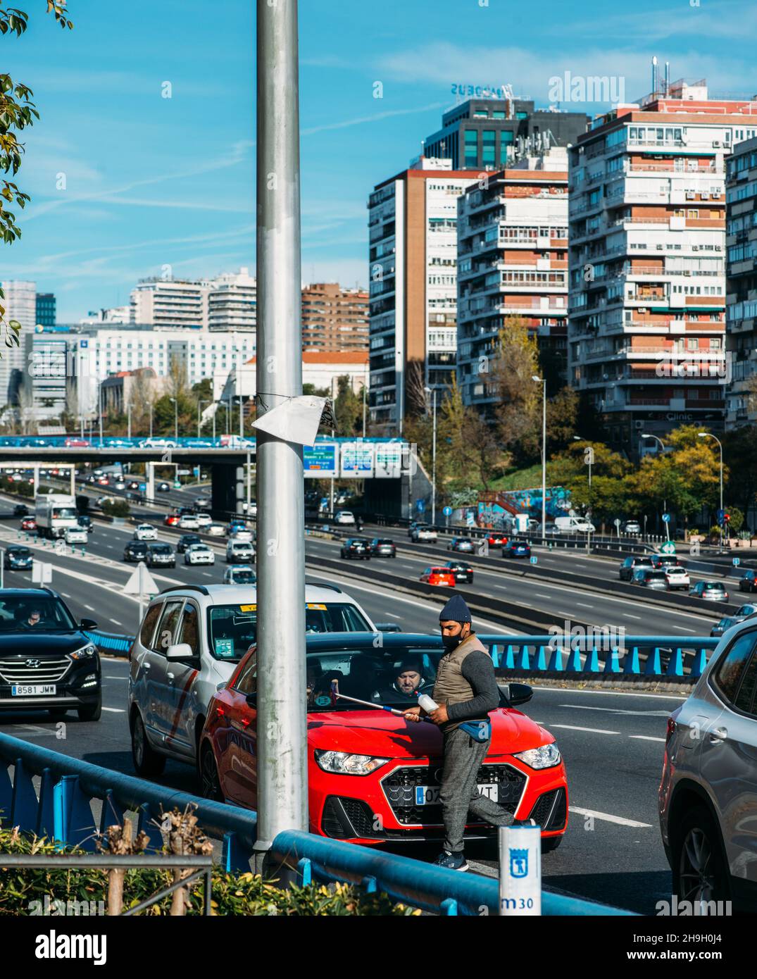 Homme d'âge moyen d'apparence sud-asiatique travaillant par lavage des vitres de voiture avec un essuie-glace (raclette) à Madrid, Espagne.Autoroute M30 Banque D'Images Homme d'âge moyen d'apparence sud-asiatique travaillant par lavage des vitres de voiture avec un essuie-glace (raclette) à Madrid, Espagne.Autoroute M30 Banque D'Images