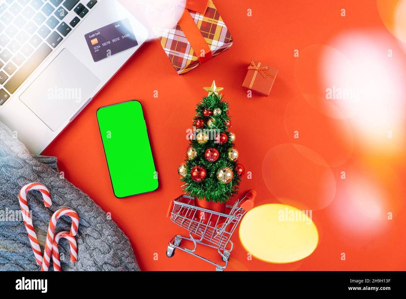 Achats en ligne de Noël sur ordinateur portable avec carte de crédit.  Décorations du nouvel an Cannes de bonbons, panier et boîte de cadeaux vue  du dessus plat couché sur fond rouge.