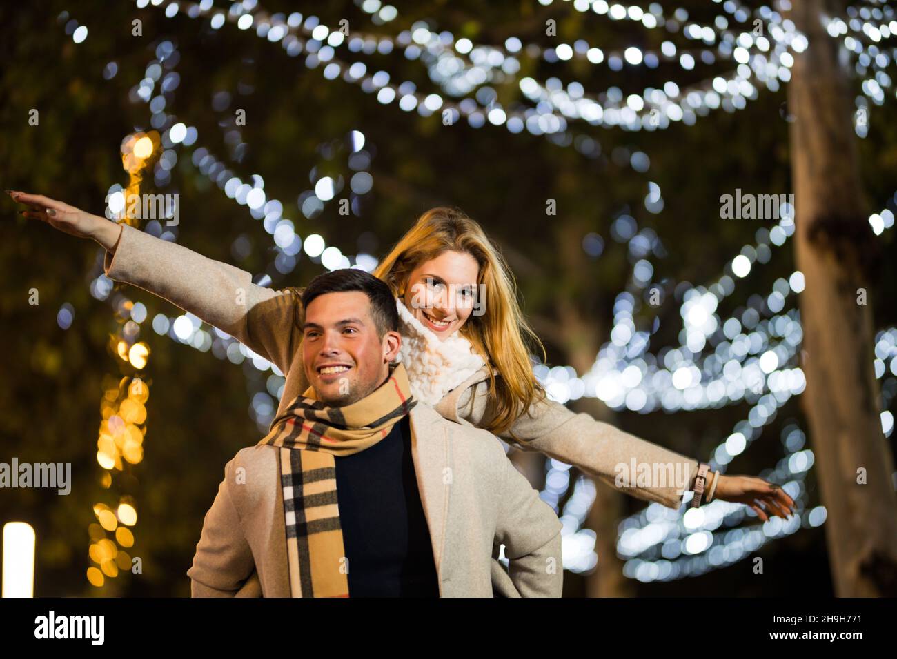 Un couple d'adolescents qui s'amusent à noël pendant la nuit dehors.Petit ami cochon petite amie avec les mains volent. Banque D'Images
