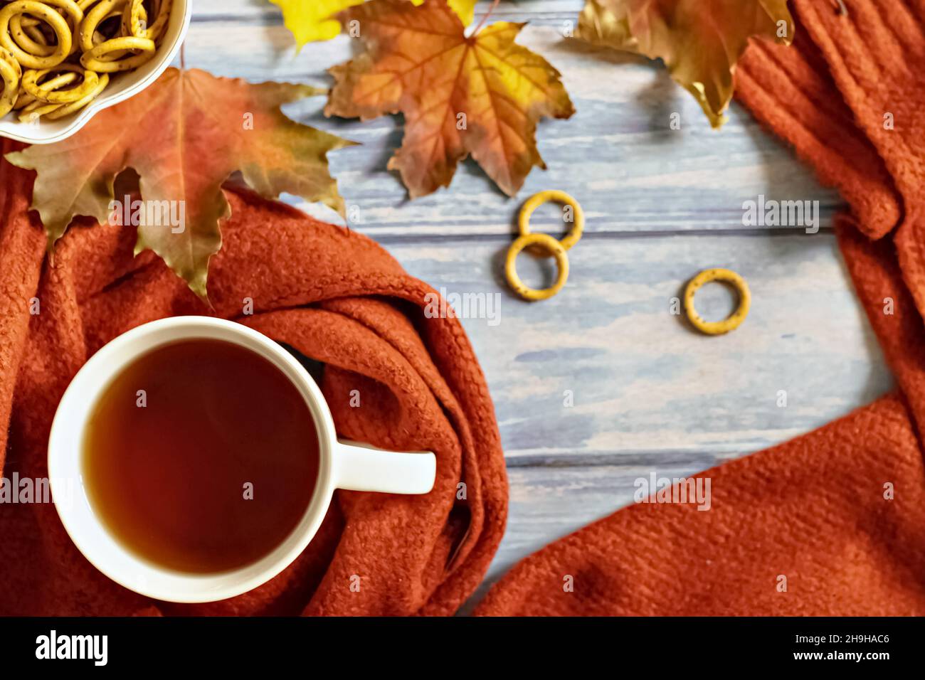 Composition d'automne, une tasse de thé chaud, une écharpe en terre cuite chaude, des feuilles mortes et un séchage sur le fond d'une table en bois bleu.Pose à plat. Banque D'Images