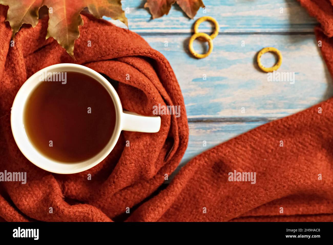 Composition d'automne, une tasse de thé chaud, une écharpe en terre cuite chaude, des feuilles mortes et un séchage sur le fond d'une table en bois bleu.Pose à plat. Banque D'Images