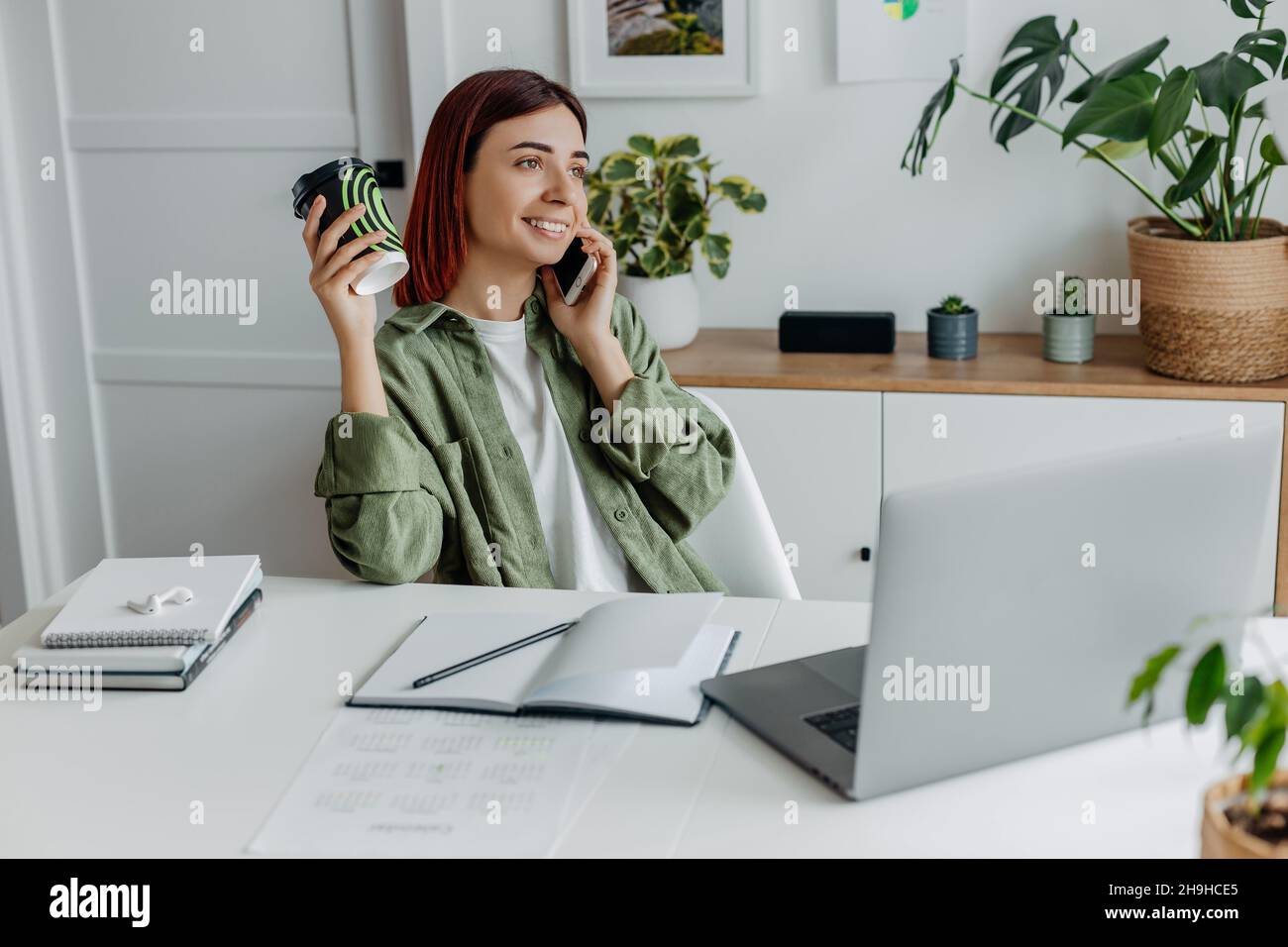 Femme travaillant à distance à la maison avec un ordinateur portable.Femme d'affaires détendue parlant au téléphone et boire du café.Concept de commerce ou de communication en ligne, gratuit Banque D'Images