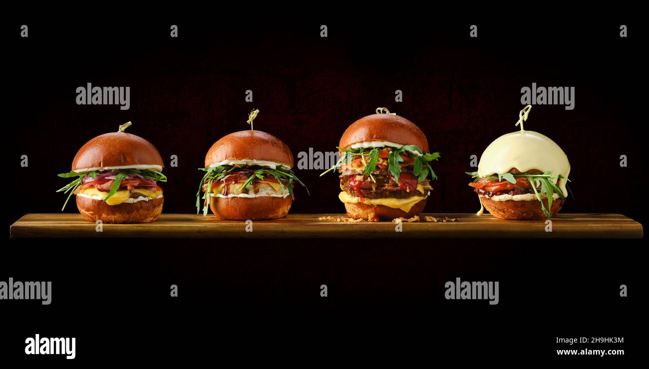 Ensemble de quatre hamburgers avec différents types de viande sur une table de service en bois Banque D'Images