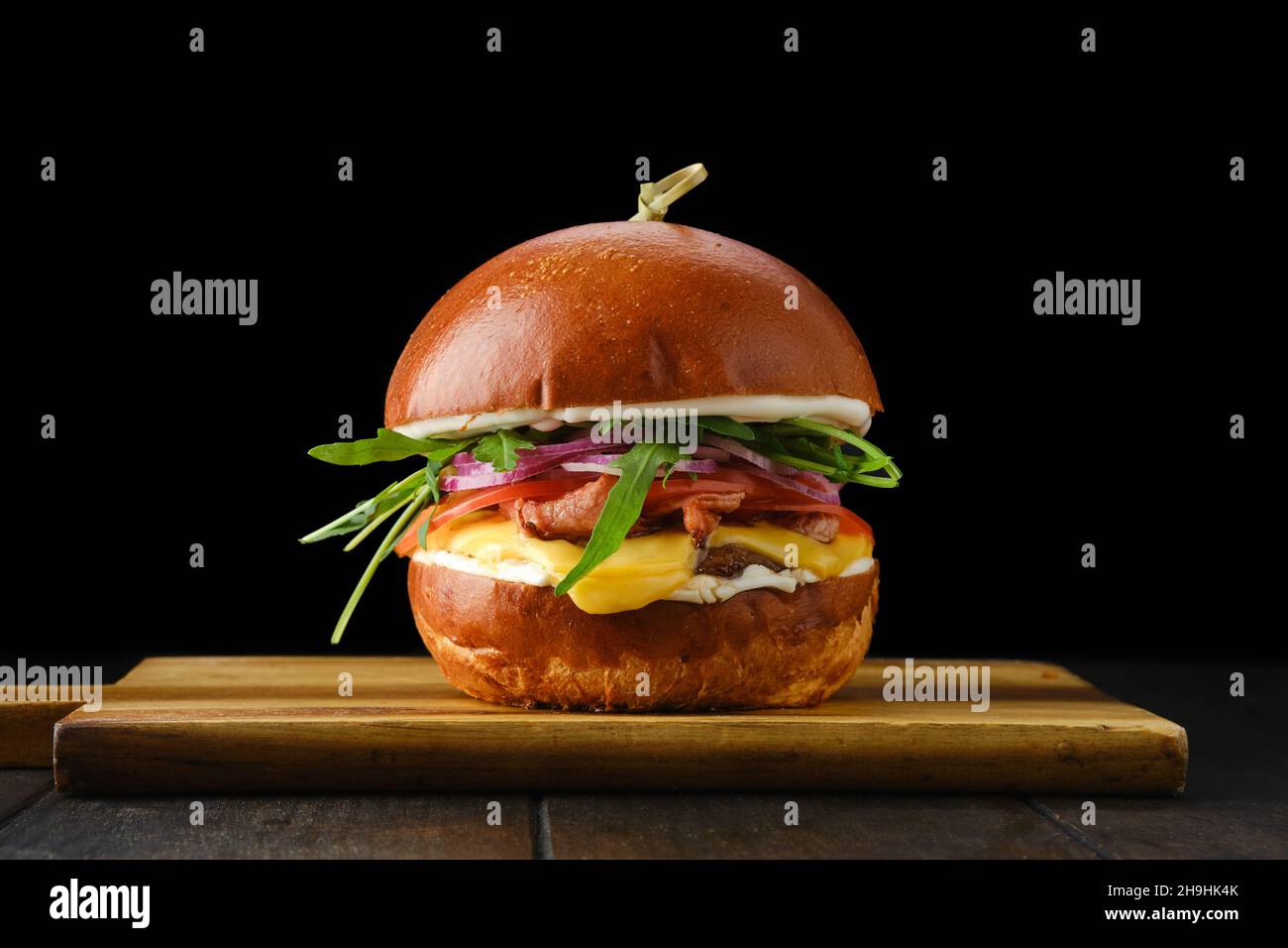 Hamburger avec bœuf et bacon croustillant sur plateau de service en bois sur fond noir Banque D'Images