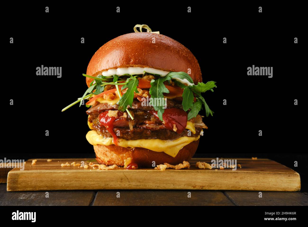 Hamburger avec deux côtelettes de bœuf et bacon sur une table de service en bois sur fond noir Banque D'Images