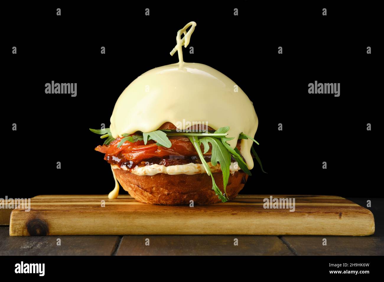 Hamburger avec bœuf et pain sur fond noir recouvert de fromage fondu sur une plaque de service en bois Banque D'Images