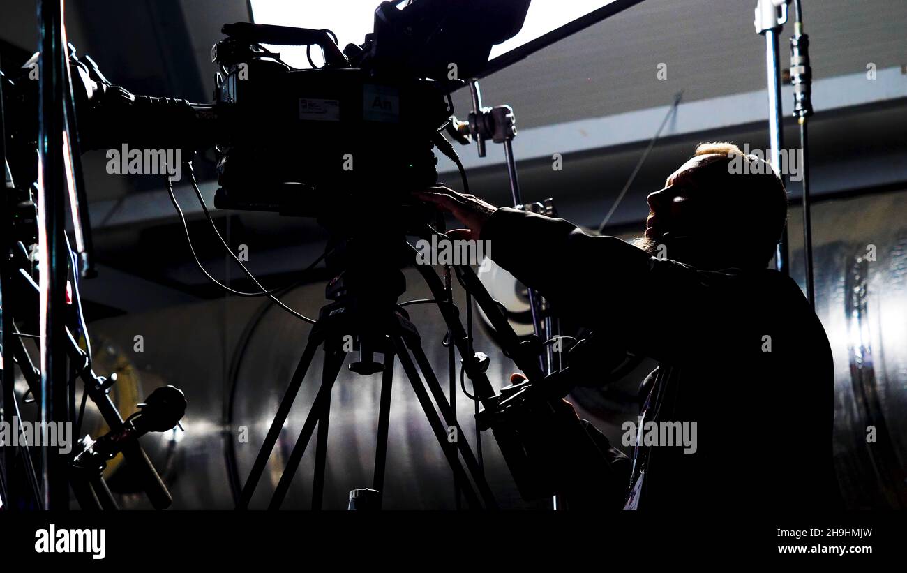 Un caméraman professionnel prend des concerts.Films.L'homme dans la nuit derrière les scènes met en place un appareil photo professionnel pour filmer un concert. Banque D'Images