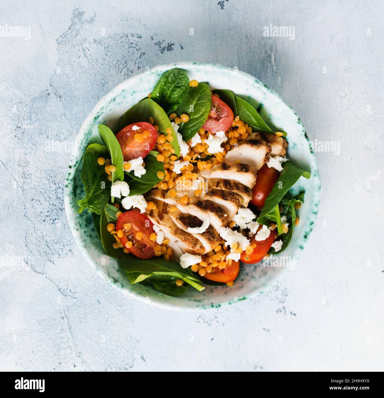 Salade avec lentilles rouges, feuilles d'épinards, tomates cerises, viande de poulet et fromage mozzarella avec huile d'olive dans une assiette de céramique sur fond gris de béton ancien Banque D'Images