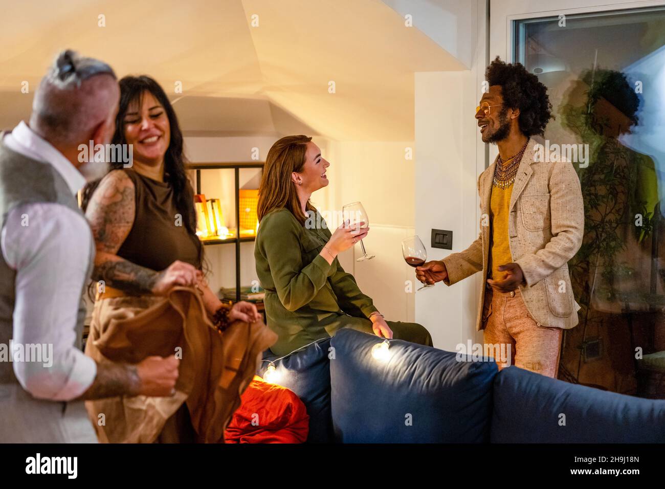 Groupe diversifié d'amis qui s'amusent, dansent et socialisent.Les adultes goûtant du vin rouge et souriant lors d'une fête privée, un groupe multiracial Banque D'Images